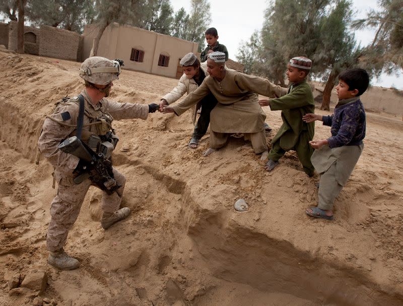FILE PHOTO: U.S. Marine Selby hands candy to local Afghan boys while keeping guard over a meeting of leaders in the Garmsir district of Helmand Province