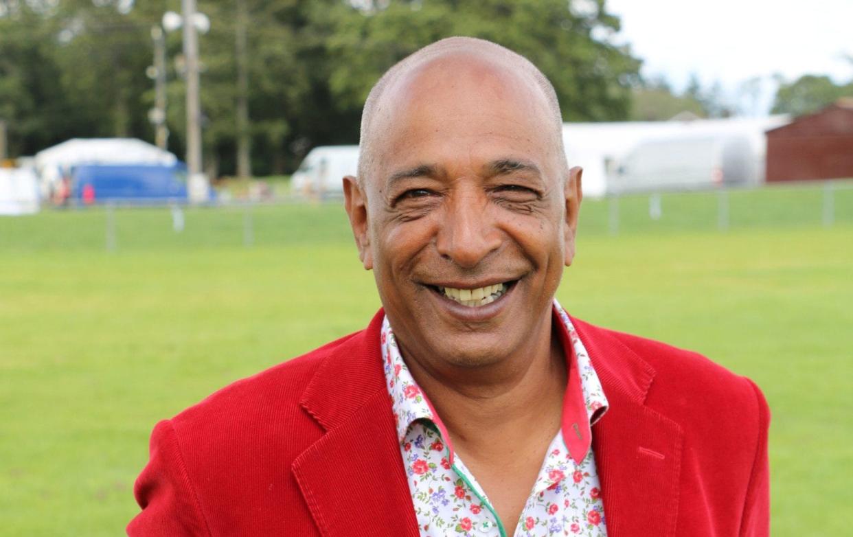 Bargain Hunt Expert Raj Bisram smiles in red suit jacket - BBC/BBC Studios