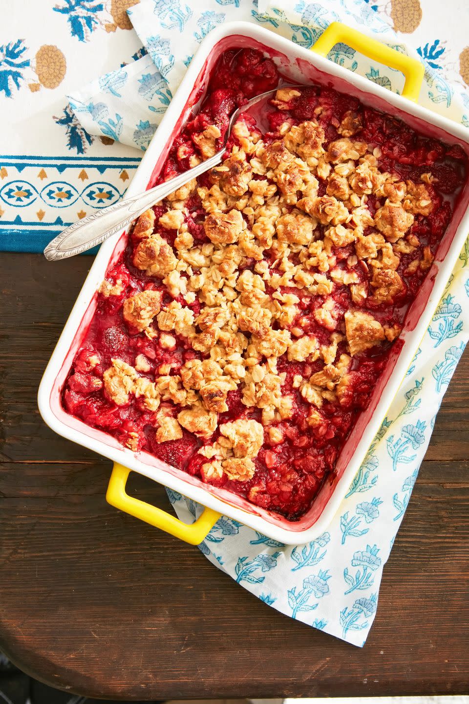 red mixed fruit crisp in a rectangle baking dish with a spoon for serving