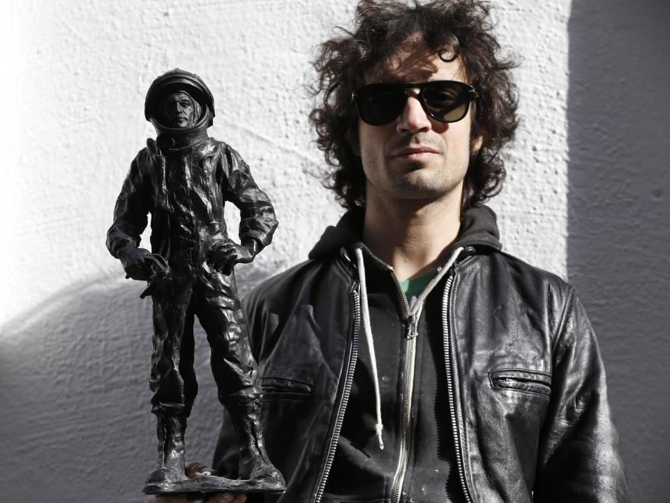 This Oct. 24, 2013 photo shows The Strokes' drummer Fabrizio Moretti with one of his cast-in-plastic astronauts beside the SoHo Rag & Bone store where his art installation in New York. Moretti's installation at one time included white niches filled with white plastic astronauts, but they were all stolen. Moretti created new black astronauts but relocated the new pieces to a second-story fire escape above the installation. (AP Photo/Kathy Willens)