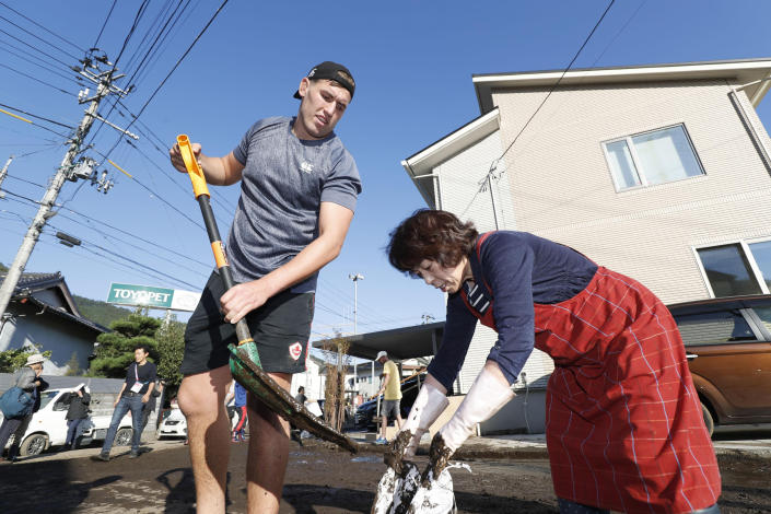 In this Oct. 13, 2019, photo, Canadian rugby player Josh Larsen, left, helps a resident to clean a road in Kamaishi, Iwate prefecture, Japan, following the cancellation of their Rugby World Cup Pool B match against Namibia due to Typhoon Hagibis. The powerful typhoon unleashed torrents of rain and strong winds Saturday that left thousands of homes on Japan's main island flooded, damaged or without power. (Kyodo News via AP)