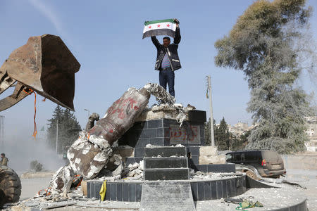 Turkish-backed Free Syrian Army member holds a flag as they pull down Kurdish statue in the center of Afrin, Syria March 18, 2018. REUTERS/Khalil Ashawi