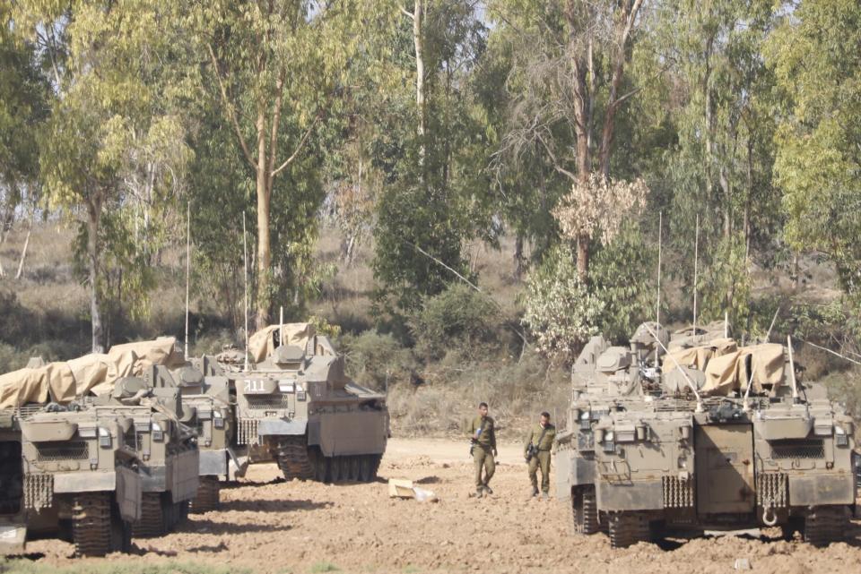 Israeli soldiers walk past military vehicles in a gathering point near the Israel-Gaza Border, Thursday, Nov. 14, 2019. Israel and the militant Islamic Jihad group in Gaza reached a cease-fire on Thursday to end the heaviest Gaza fighting in months. (AP Photo/Ariel Schalit)
