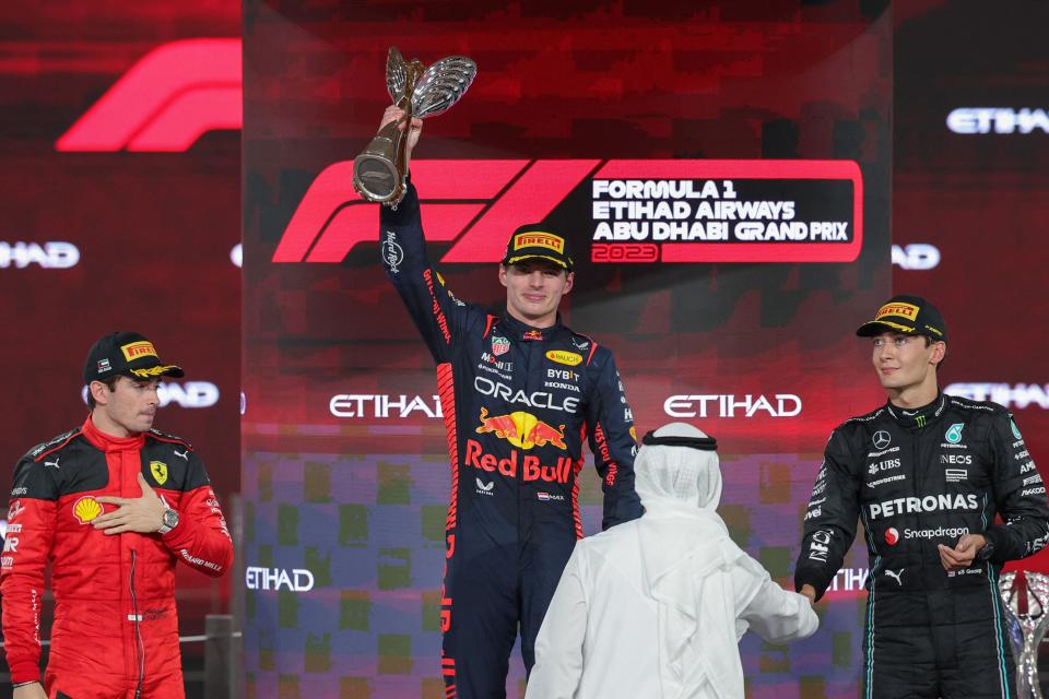 Ferrari's Monegasque driver Charles Leclerc (L) and Mercedes' British driver George Russell (R) watch as Red Bull Racing's Dutch driver Max Verstappen celebrates with the winners trophy on the podium after the Abu Dhabi Formula One Grand Prix at the Yas Marina Circuit in the Emirati city on November 26, 2023.