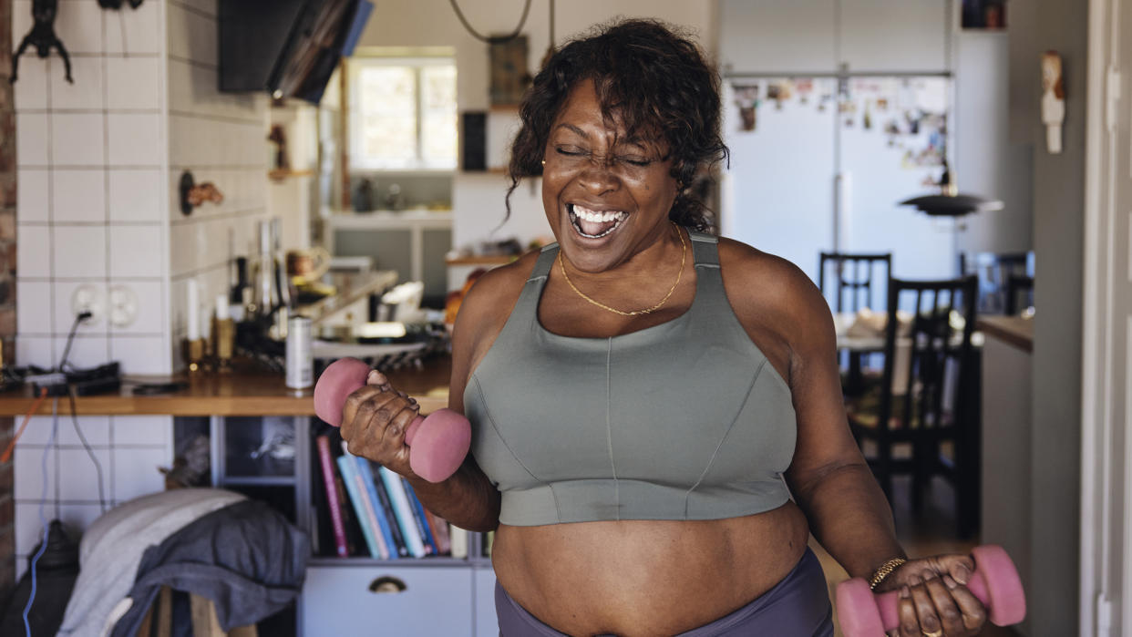  Joyful middle aged woman working out at home with dumbbells. 