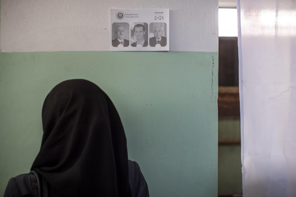 A Syrian woman stands in front of a sample ballot prior to voting in a presidential election, at a polling station in the town of Douma, near the Syrian capital Damascus, Syria, Wednesday, May 26, 2021. Syrians headed to polling stations early Wednesday to vote in the second presidential elections since the deadly conflict began in the Arab country. (AP Photo/Hassan Ammar)