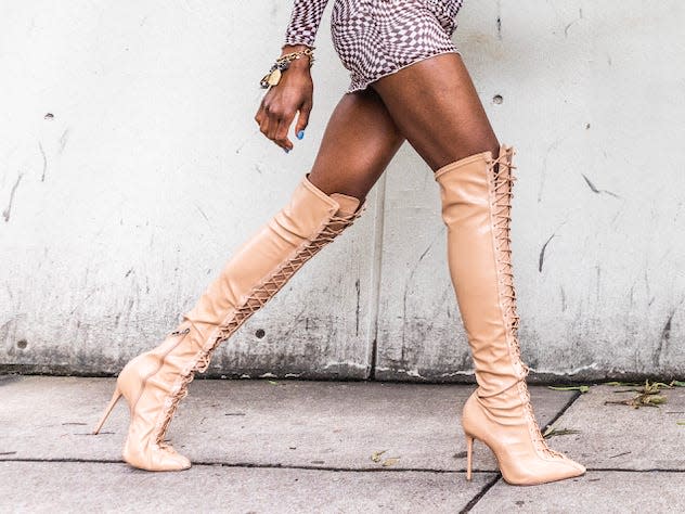 woman walking down a sidewalk wearing a tight dress and tight knee-high boots