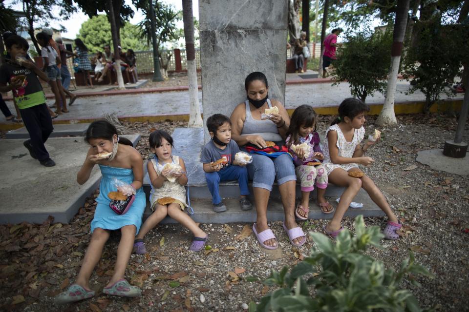 Children eat free arepas or corn flour patties, given to them by Andres Burgos, a 55-year-old publicist, in Macuto, Venezuela, Saturday Oct. 24, 2020. Burgos, who is on a mission to feed the hungry, rode to the seaside city in Venezuela's La Guaira state, accompanied by other cyclists to distribute the arepas he made to needy children, adults and the elderly. (AP Photo/Ariana Cubillos)