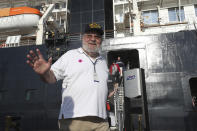 A passenger of the MS Westerdam, owned by Holland America Line, cheers after they disembark from the MS Westerdam, back, at the port of Sihanoukville, Cambodia, Saturday, Feb. 15, 2020. After being stranded at sea for two weeks because five ports refused to allow their cruise ship to dock, the passengers of the MS Westerdam were anything but sure their ordeal was finally over. (AP Photo/Heng Sinith)