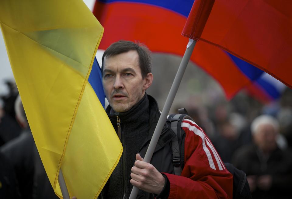 A demonstrator carries Russian and Ukrainian flags during a march to oppose president Vladimir Putin's policies in Ukraine, in Moscow, Saturday, March 15, 2014. Large rival marches have taken place in Moscow over Kremlin-backed plans for Ukraine’s province of Crimea to break away and merge with Russia. More than 10,000 people turned out Saturday for a rally in the center of the city held to oppose what many demonstrators described as Russia’s invasion of the Crimean Peninsula. In a nearby location, a similar sized crowd voiced its support for Crimea’s ethnic Russian majority, who Moscow insists is at threat from an aggressively nationalist leadership now running Ukraine. (AP Photo/Alexander Zemlianichenko)