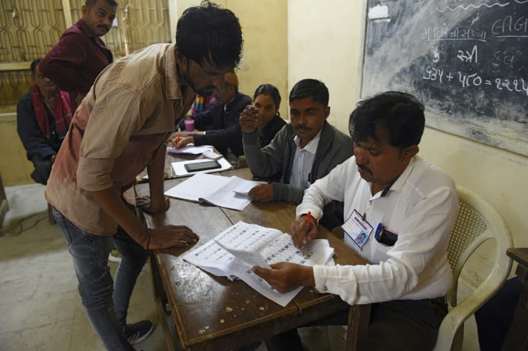 Indian officials verify documents of voters before casting their ballots during the first phase of Vidhan Sabha elections of Gujarat state in Limbdi, some 100 kms from Ahmedabad