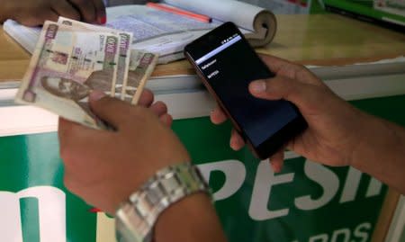 A customer conducts a mobile money transfer, known as M-Pesa, at a Safaricom agent stall, as he holds Kenyan shillings (KSh) in Nairobi, Kenya October 16, 2018. REUTERS/Thomas Mukoya