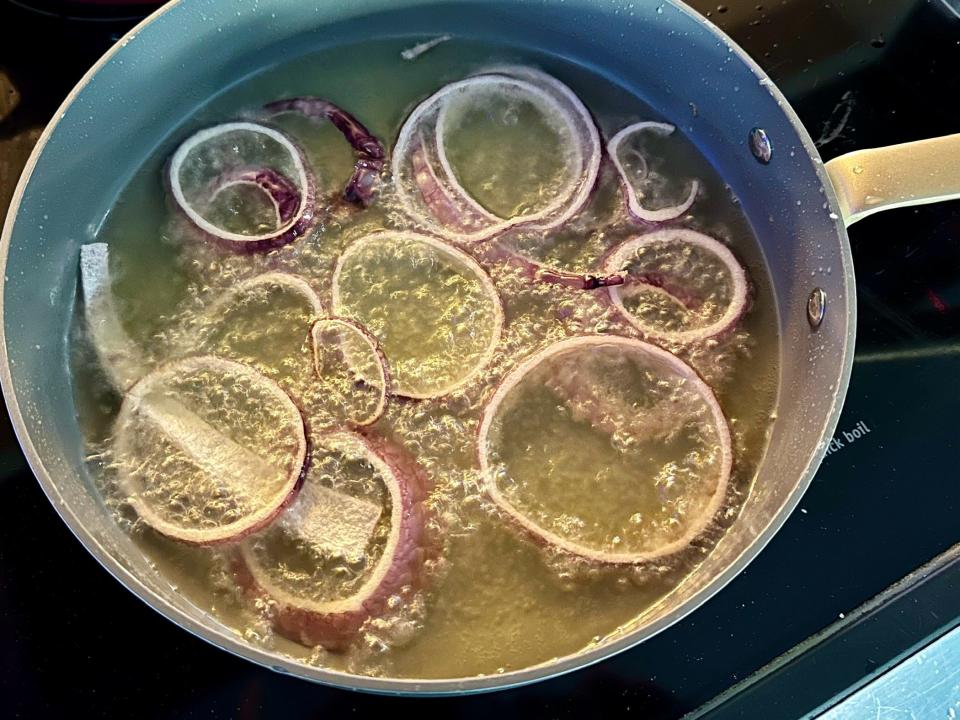 red onions frying in oil in a pan