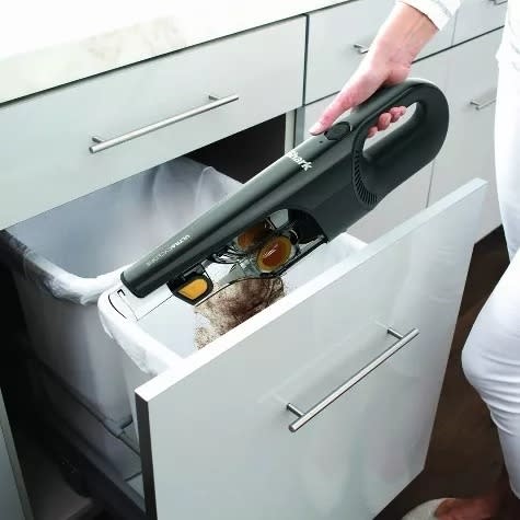 A handheld vacuum being emptied into the trash