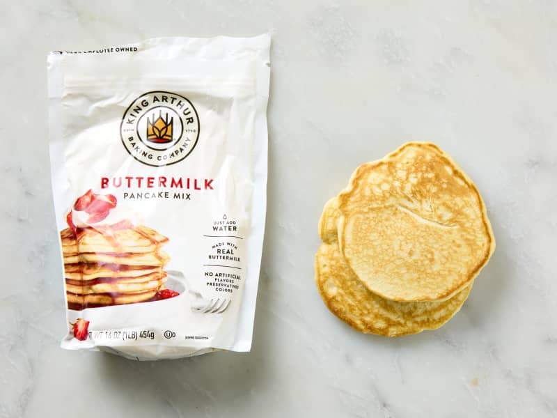 overhead shot of a bag of king arthur baking company pancake mix, with two pancakes to the right of it.