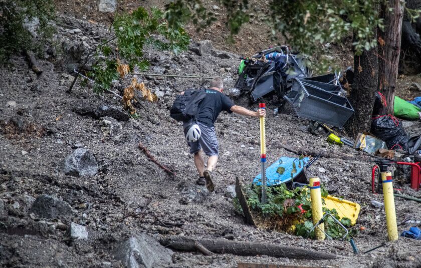 FOREST FALLS, CA - SEPTEMBER 12, 2022: Homeowner Olin Richie steadies himself on a metal pole while trying to hike up to his house through mud and debris after heavy rain created a large mudslide on Canyon Drive on September 12, 2022 in Forest Falls, California. (Gina Ferazzi / Los Angeles Times)