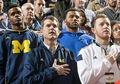 Michigan football head coach Jim Harbaugh, center, stands for the national anthem with son Jay, right, and recruits, before an NCAA college basketball game against Northwestern at Crisler Center in Ann Arbor, Mich., Saturday, Jan. 17, 2015. (AP Photo/Tony Ding)