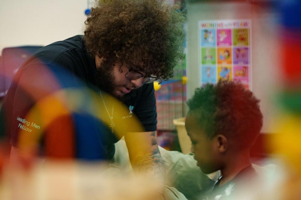 Seen past a colorful bead maze toy, Leading Men fellow De'Von Stewart sits on the ground with Josiah Miller, 4, as they play with plastic building toys at Desert Garden Preschool in Glendale on Sept. 21, 2023.