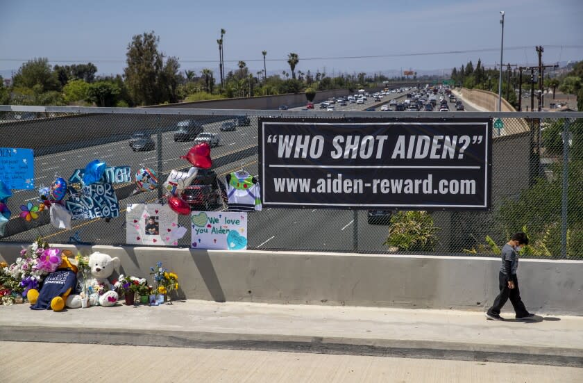 Orange, CA - May 27: Six-year-old Victor Flores, of Orange, walks alone clutching a Pokemon card for comfort, ahead of his family, where his dad said he was sad because he is the same age as 6-year-old shooting victim Adrian Leos, where they prayed and left flowers at a growing makeshift memorial on the Walnut Ave. overpass of the 55 Freeway in Orange May 27, 2021. The memorial featured balloons, toys, cards, messages of love and candles to remember a 6-year-old boy who was shot and killed Friday during an apparent road rage incident on the 55 Freeway. New banners have been placed on the overpass as officials and community continue to increase the reward for arrest of the killer and accomplice. (Allen J. Schaben / Los Angeles Times)