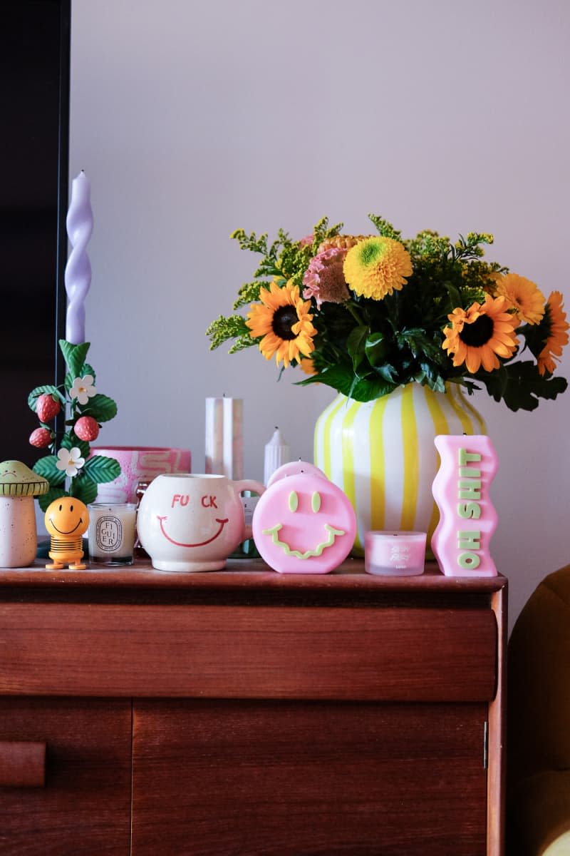 Pink candles and yellow striped vase decorate media cabinet.