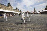 Volunteers wearing face masks, gloves and protective gear to protect against coronavirus, preapre to clean an area of an outdoor book market set up at Red Square with GUM, State Department store, left, St. Basil's Cathedral, center, Spasskaya Tower, second with, and the Kremlin Wall, right, in Moscow, Russia, Saturday, June 6, 2020. Muscovites clad in face masks and gloves ventured into Red Square for an outdoor book market, a small sign of the Russian capital's gradual efforts to open up amid coronavirus concerns. (AP Photo/Alexander Zemlianichenko)