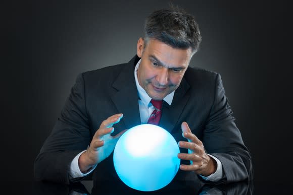 Man in a suit looks into a bright blue crystal ball.