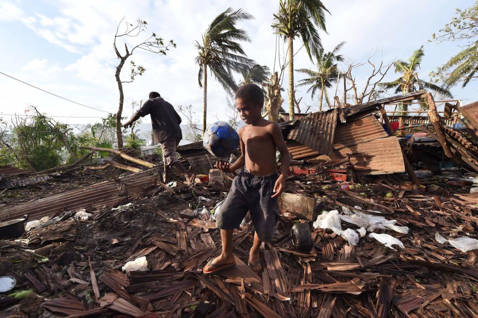 Samuel, only his first name given, carries a ball through the ruins of their family home as his father, Phillip, at back, picks through the debris in Port Vila, Vanuatu in the aftermath of Cyclone Pam Monday, March 16, 2015.