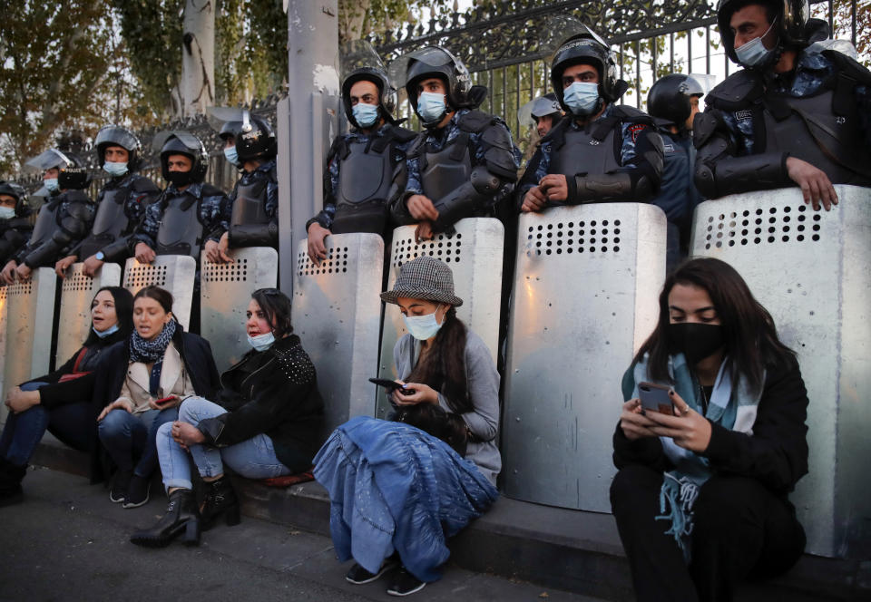 Women sit as police guard the parliamentary building, during a protest against an agreement to halt fighting over the Nagorno-Karabakh region, in Yerevan, Armenia, Wednesday, Nov. 11, 2020. Thousands of people flooded the streets of Yerevan once again on Wednesday, protesting an agreement between Armenia and Azerbaijan to halt the fighting over Nagorno-Karabakh, which calls for deployment of nearly 2,000 Russian peacekeepers and territorial concessions. Protesters clashed with police, and scores have been detained. (AP Photo/Dmitri Lovetsky)