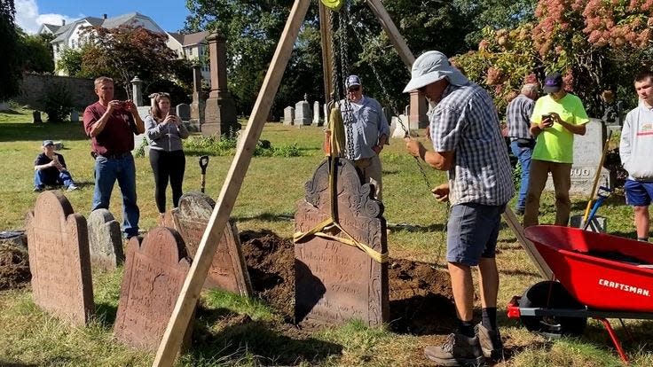 Pictured is Jon Appell resetting a tablet stone with the help of an overhead tripod, during a cemetery preservation workshop.