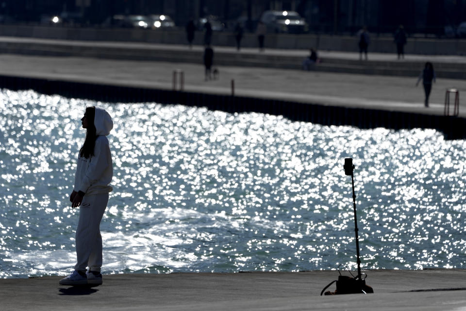 A lone woman creates a social media video along Lake Michigan Monday, Feb. 26, 2024, in Chicago. A warm front is sweeping spring-like weather across a large swath of the country in what is usually one of the coldest months of the year. The rare warmup is sending people out of their homes to enjoy the winter respite but also bringing increased wildfire danger. (AP Photo/Charles Rex Arbogast)