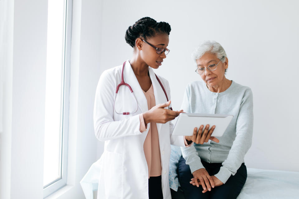 Dr. Sinha encourages senior women to advocate for their health and ask for a specialists if they feel like something's not right. (Getty) A black female doctor standing next to female patient and showing her something on digital tablet.
