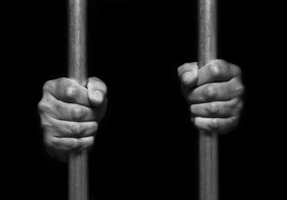 Person's hands holding prison bars. (PHOTO: Getty Images)