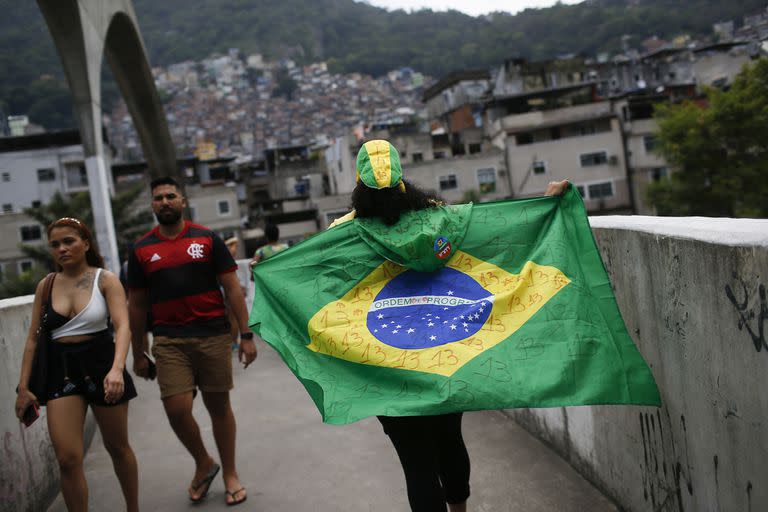 Una mujer camina con una bandera de Brasil en la favela Rocinha durante la segunda vuelta de las elecciones presidenciales en Río de Janeiro, Brasil, domingo 30 de octubre de 2022. 