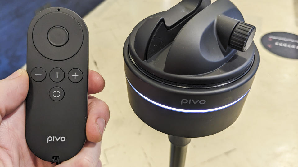 Pivo Max remote in the hand, with Pivo Max on a stand in the background