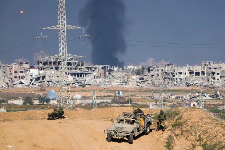 Soldados israelíes toman posiciones cerca de la frontera de la Franja de Gaza, mientras al fondo una columna de humo marca el lugar donde se produjo un ataque aéreo israelí en el enclave palestinos, visto desde el sur de Israel, el 29 de diciembre de 2023. (AP Foto/Ariel Schalit)