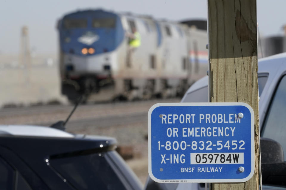 A sign is shown at a railroad crossing, Sunday, Sept. 26, 2021, near to cars from an an Amtrak train that derailed Saturday just west of Joplin, Mont. The westbound Empire Builder was en route to Seattle from Chicago, with two locomotives and 10 cars. (AP Photo/Ted S. Warren)