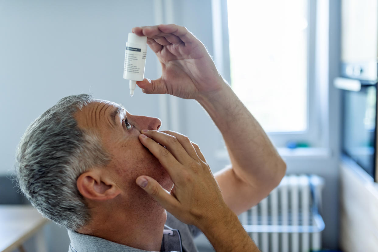 Photo of a mature man putting eye drop. Close-up Of A Mature Man Putting Eye Drops In dry Eyes. Gray hair Man putting eye drop. Closeup view of an elderly person using a bottle of eyedrops in her eyes, sick old man suffering from the irritated eye. optical symptoms, health concept.