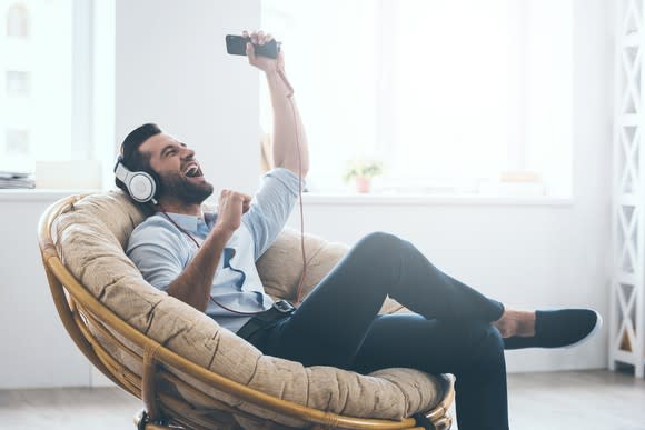 A man sitting in a chair listening to music on his phone.