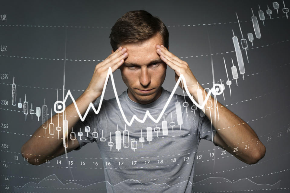 Man with hands on side of his head and a stock chart in the foreground.