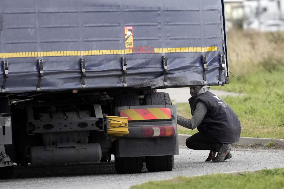 A migrant tries to hide on a truck in Calais, northern France, Thursday, Oct. 14, 2021, to cross the tunnel heading to Britain. In a dangerous and potentially deadly practice, he is trying to get through the heavily policed tunnel linking the two countries by hiding on a truck. (AP Photo/Christophe Ena)