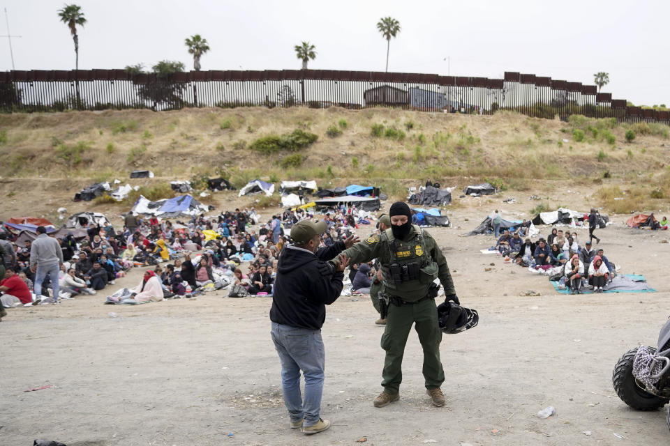 A man jokes with a U.S. Border Patrol agent as he and other migrants wait between two border walls to apply for asylum Friday, May 12, 2023, in San Diego. Hundreds of migrants remain waiting between the two walls, many for days. The U.S. entered a new immigration enforcement era Friday, ending a three-year-old asylum restriction and enacting a set of strict new rules that the Biden administration hopes will stabilize the U.S.-Mexico border and push migrants to apply for protections where they are, skipping the dangerous journey north. (AP Photo/Gregory Bull)