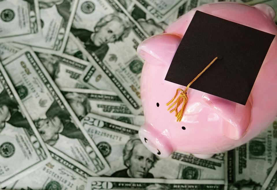 Piggy bank with graduation cap on pile of money