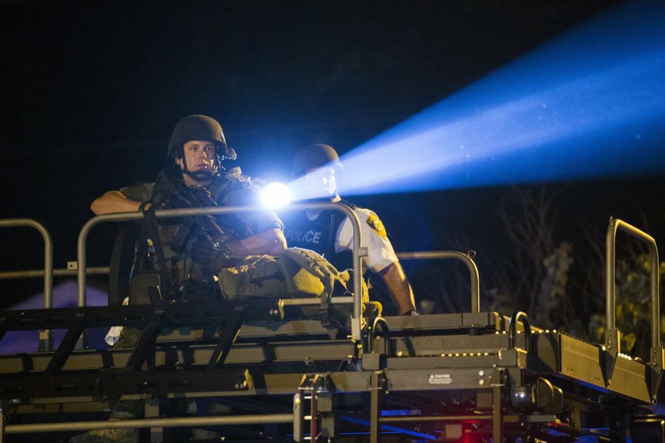 A police officer points a spotlight at a more vocal and confrontational group of demonstrators during further protests in reaction to the shooting of Michael Brown, near Ferguson, Missouri August 18, 2014. Police fired tear gas and stun grenades at protesters in Ferguson, Missouri on Monday, after days of unrest sparked by the fatal shooting of an unarmed black teenager by a white policeman. REUTERS/Lucas Jackson (UNITED STATES - Tags: CIVIL UNREST CRIME LAW TPX IMAGES OF THE DAY)