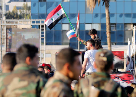 A Syrian soldier waves Russian and Syrian flags during a protest against air strikes in Damascus,Syria April 14,2018.REUTERS/ Omar Sanadiki