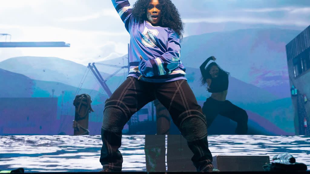 sza holding her microhpone in the air with her right arm as she dances during a concert