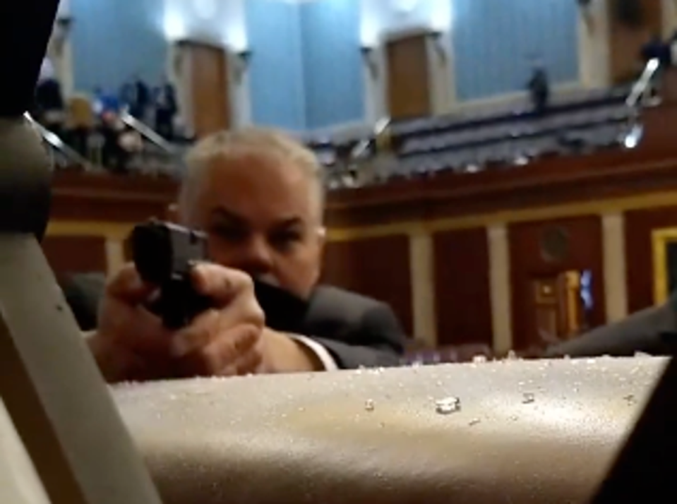 A security guard points his firearm at rioters storming the US Capitol on 6 January 2021 in footage captured on a cellphone (NBC News)