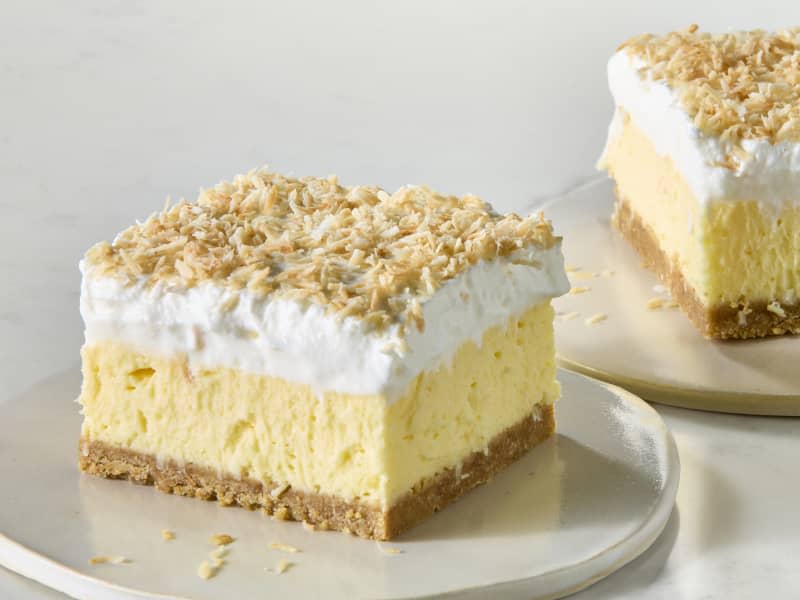 angled shot of a slice of coconut delight, on a small flat white plate, with another slice in the background.