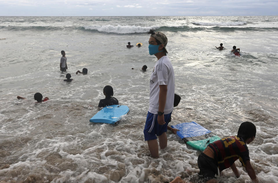 A boy wearing a face mask for curbing the spread of coronavirus plays in the surf at a beach in Bali, Indonesia on Wednesday, Nov. 25, 2020. (AP Photo/Firdia Lisnawati)