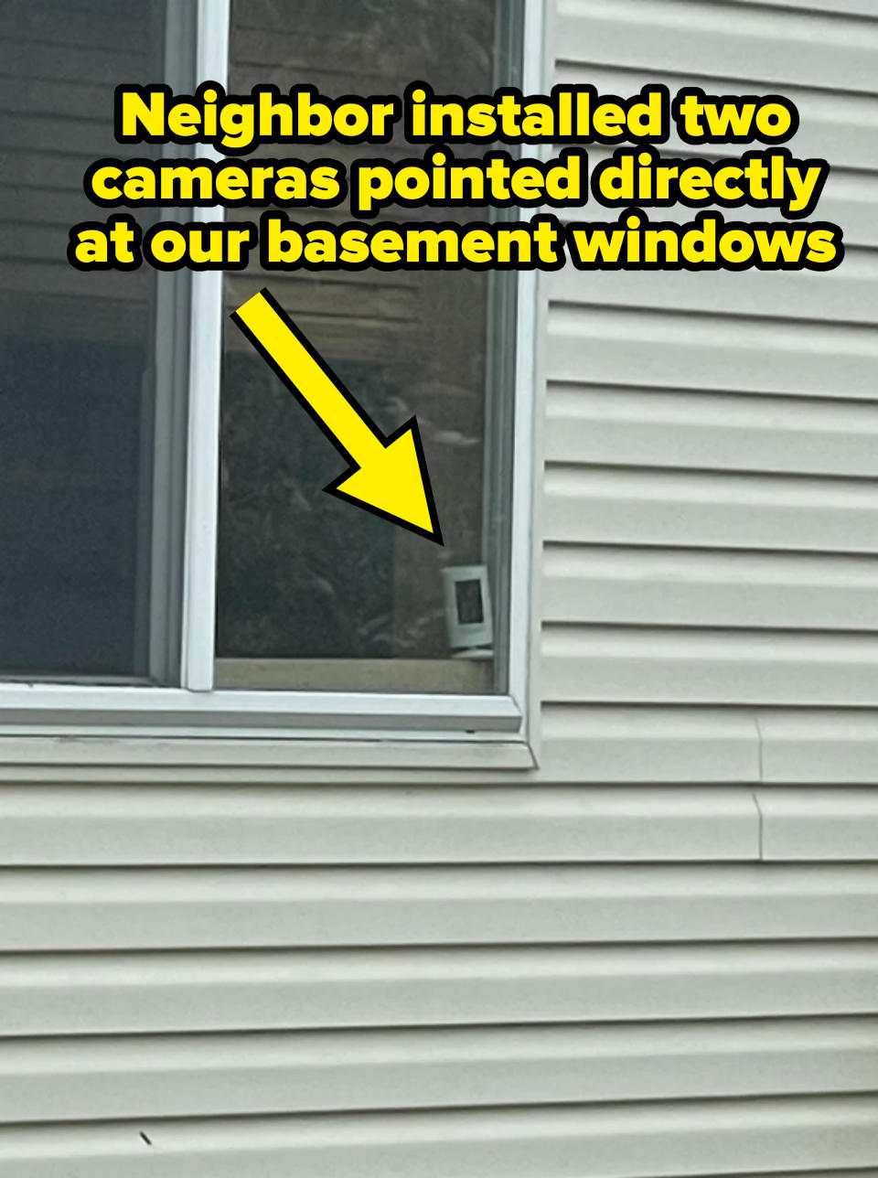 A house's exterior with a window and white siding. Inside the window, a small framed photo sits on the windowsill