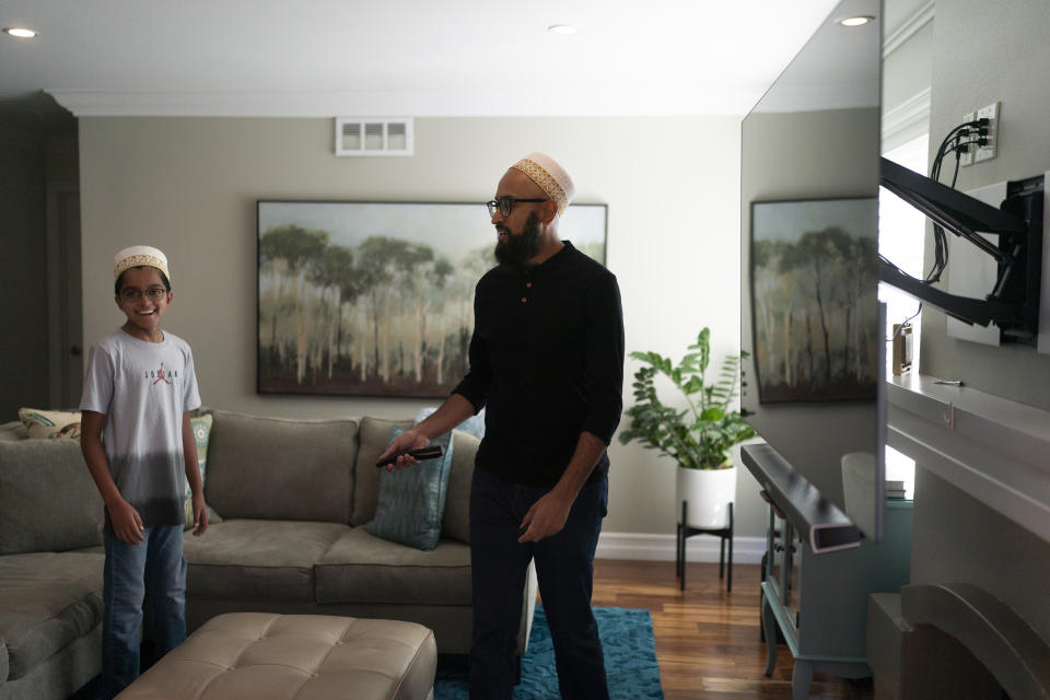 Yusuf Zakir, center, shares a light moment with his son, Burhanuddin, as he turns on a TV to watch an episode of "Ms. Marvel" in Anaheim, Calif., Friday, July 8, 2022. The new Ms. Marvel series on Disney Plus has resonated with Muslims in the West. The show's refreshing approach to portraying the everyday lives of American Muslims has won many hearts. (AP Photo/Jae C. Hong)